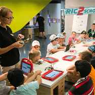 Trainerin und Kinder vor Tablets im Rahmen eines RIC2School Workshops