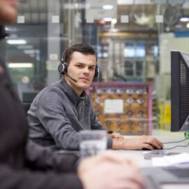 Mitarbeiter an einem Büroarbeitsplatz, vor einem Computerbildschirm mit einem Headset auf